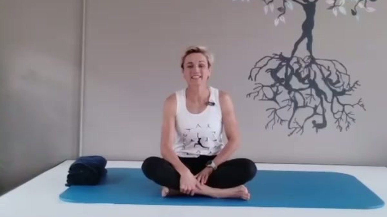 Jou instrukteur glimlag en sit kruisbeen op ’n Pilates-mat